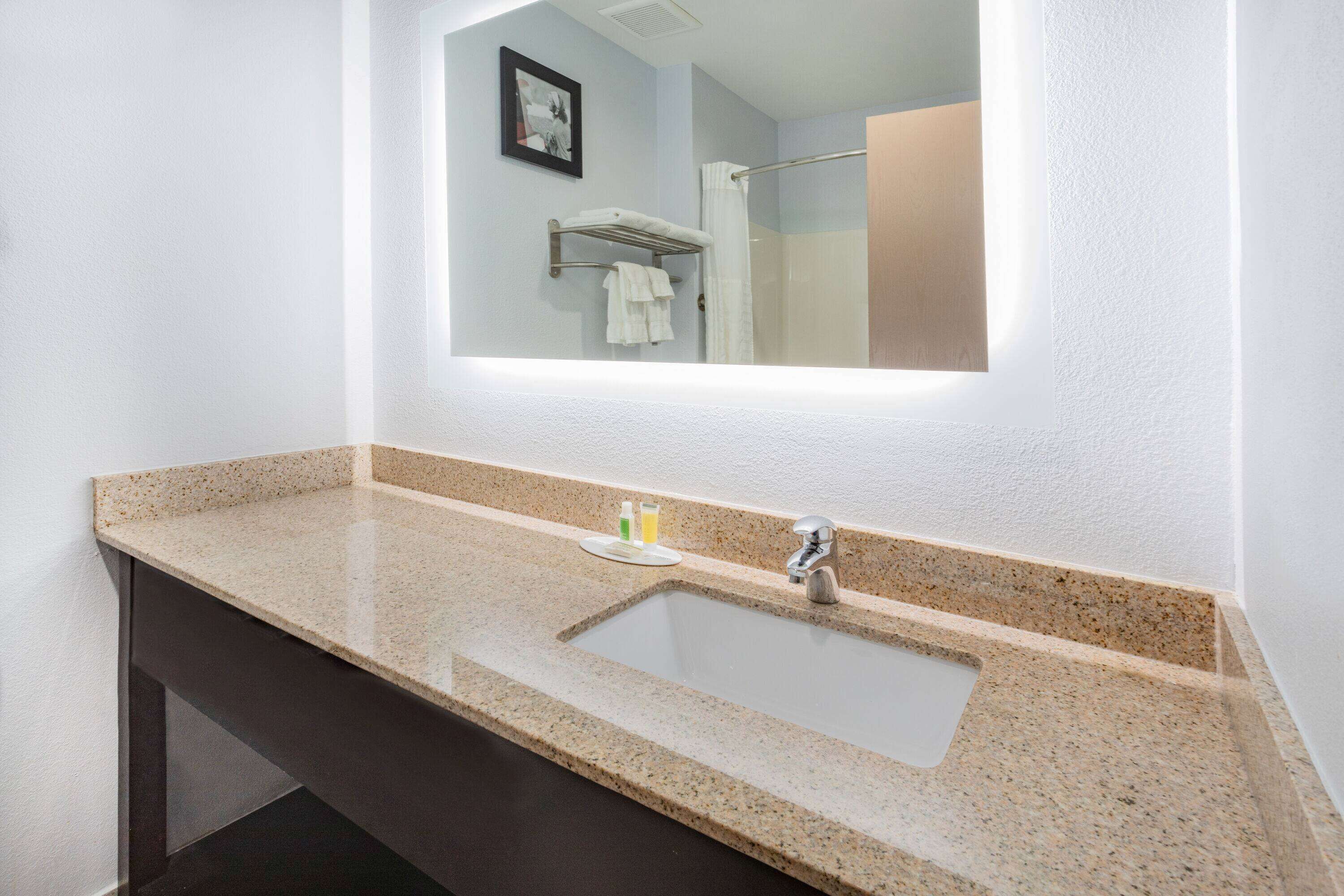 A bathroom with a granite countertop sink, a mirror, and a towel rack.