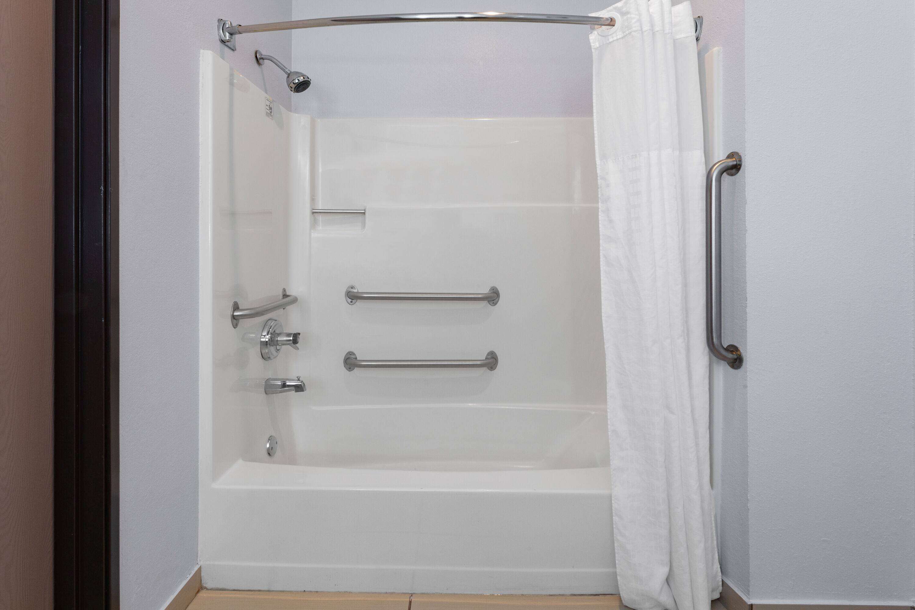 A white bathtub with a showerhead, grab bars, and a curtain.