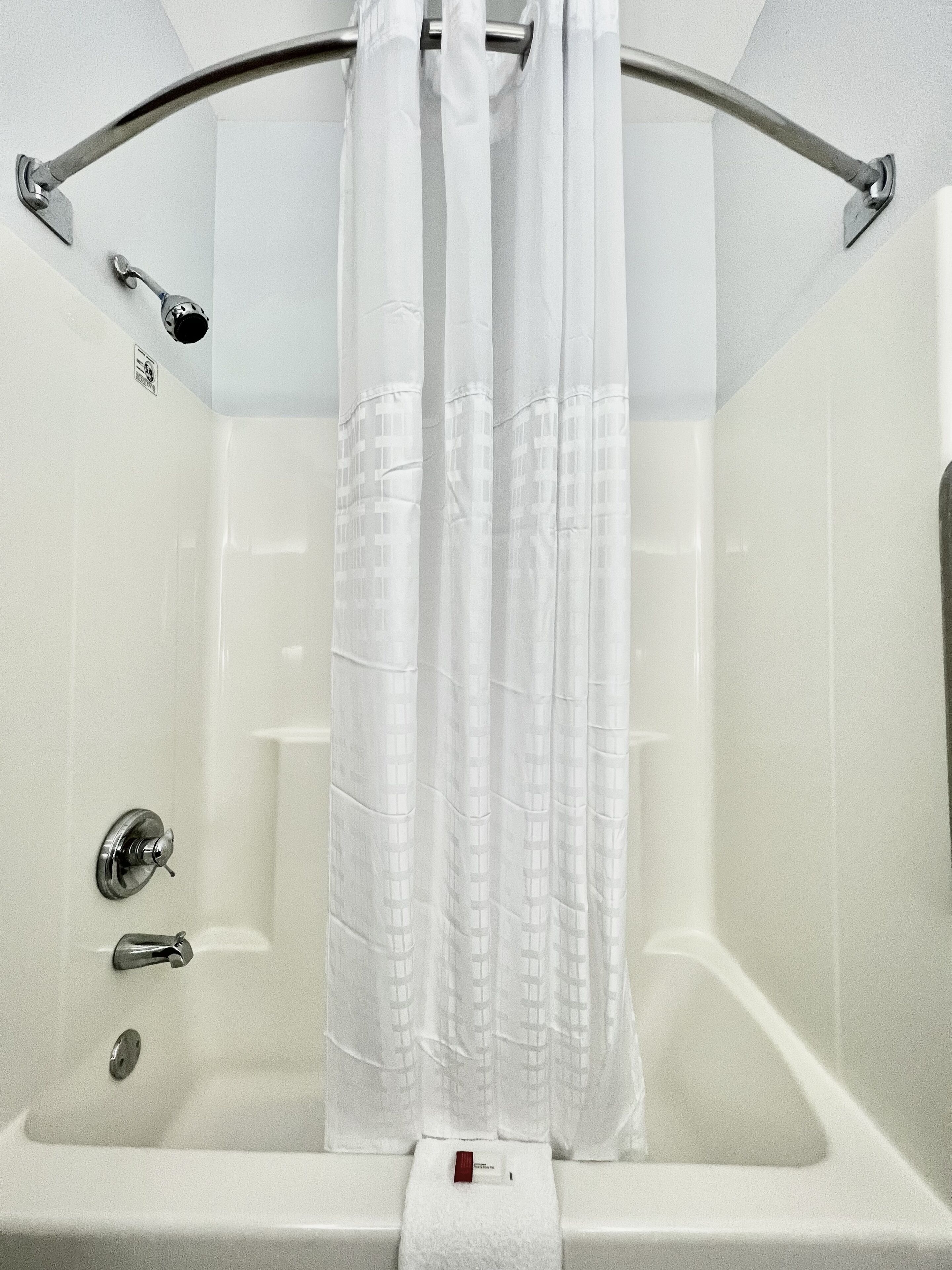 Une baignoire blanche avec un rideau de douche, une douchette et un porte-serviettes.