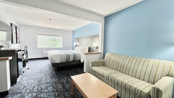Habitación de hotel con cama, sofá, escritorio y ventana con vista a árboles.