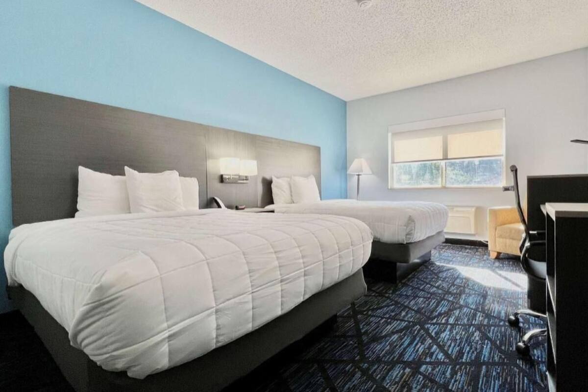 A hotel room with two beds, a desk, a chair, and a window.