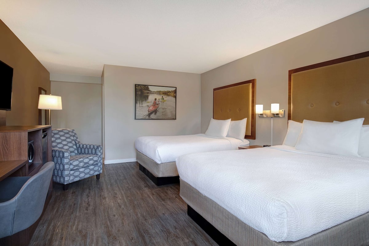 Ein Hotelzimmer mit zwei Betten, einem Schreibtisch, einem Sessel und einem Bild an der Wand.