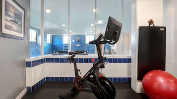 Una bicicleta estática, una pelota de ejercicios roja y un refrigerador en una habitación con piso y paredes de baldosas azules y blancas.