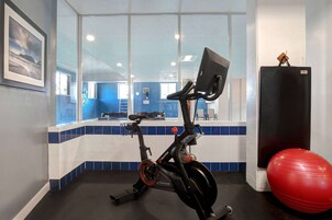 Una bicicleta estática, una pelota de ejercicios roja y un refrigerador en una habitación con piso y paredes de baldosas azules y blancas.