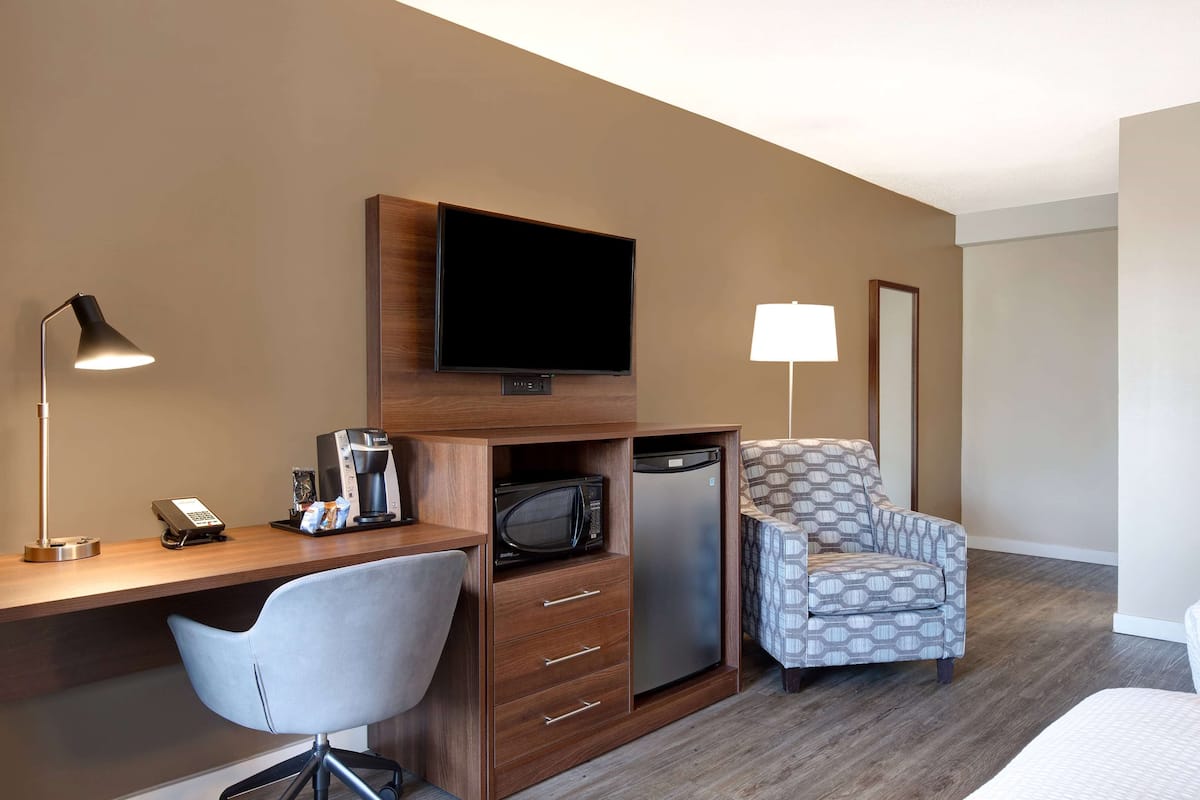 Ein Hotelzimmer mit Schreibtisch aus Holz, Fernseher, Mikrowelle, Kühlschrank, Stuhl und Lampe.
