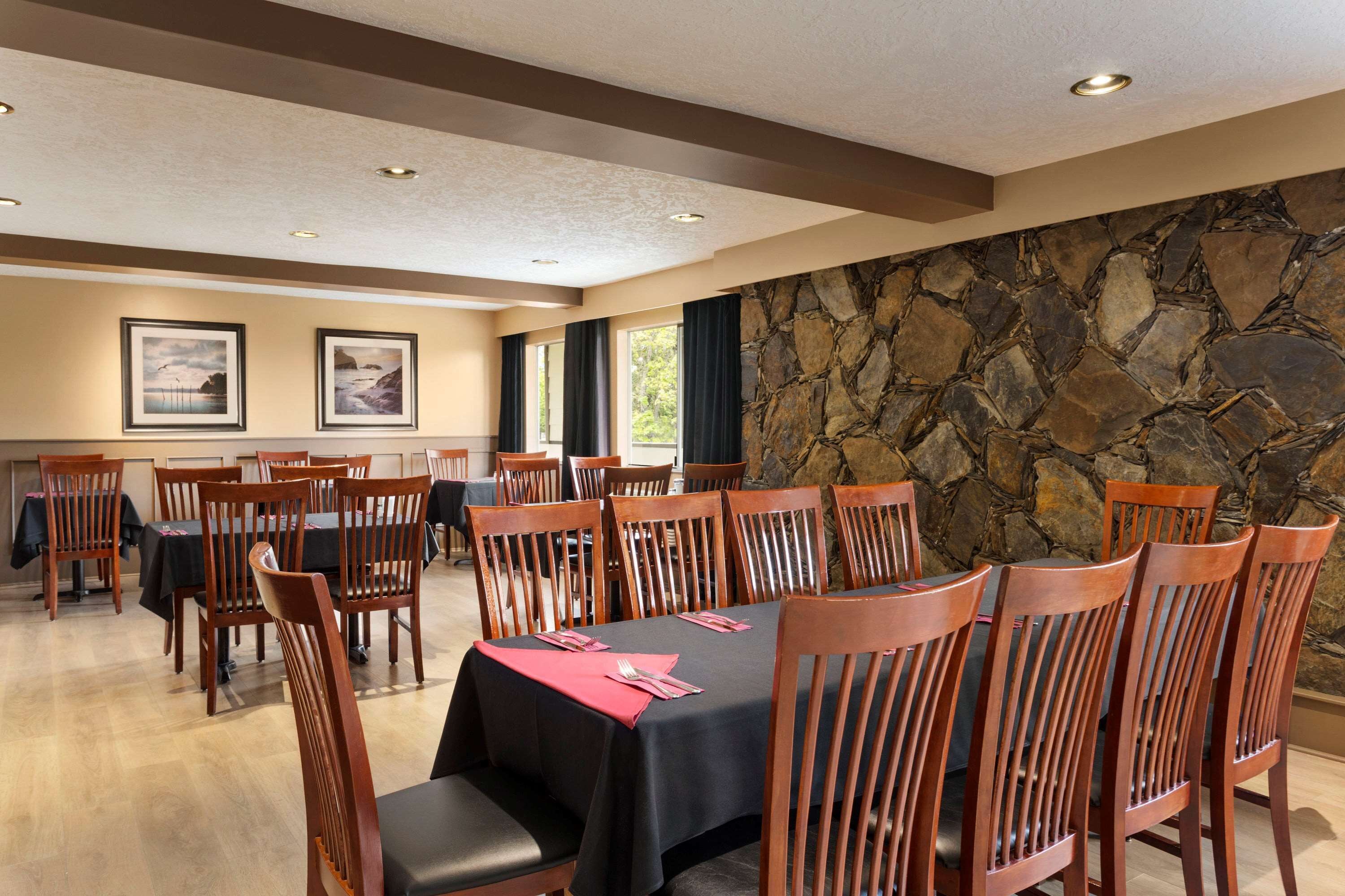 A dining area with multiple tables and chairs, a stone wall, and framed pictures on the wall.