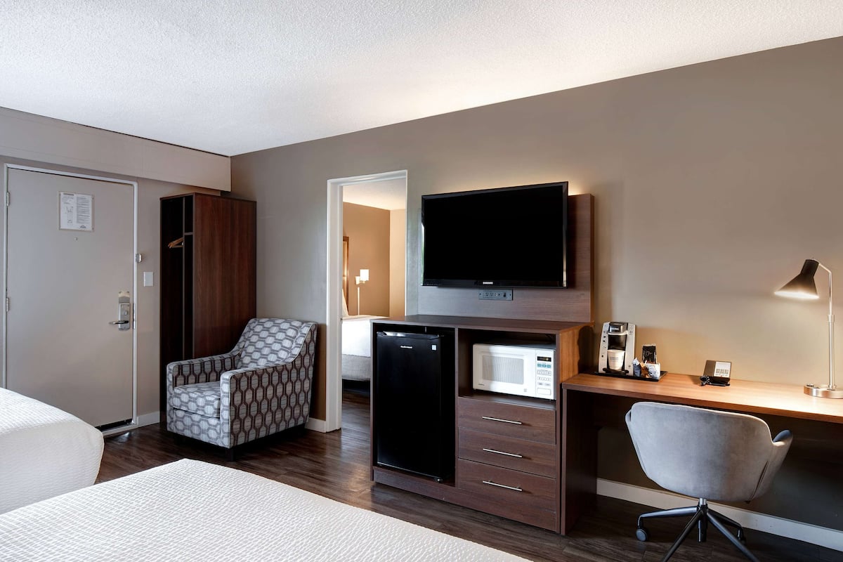 Ein Hotelzimmer mit einem Bett, einem Schreibtisch mit Computer, einem Fernseher, einer Mikrowelle und einem Kühlschrank.