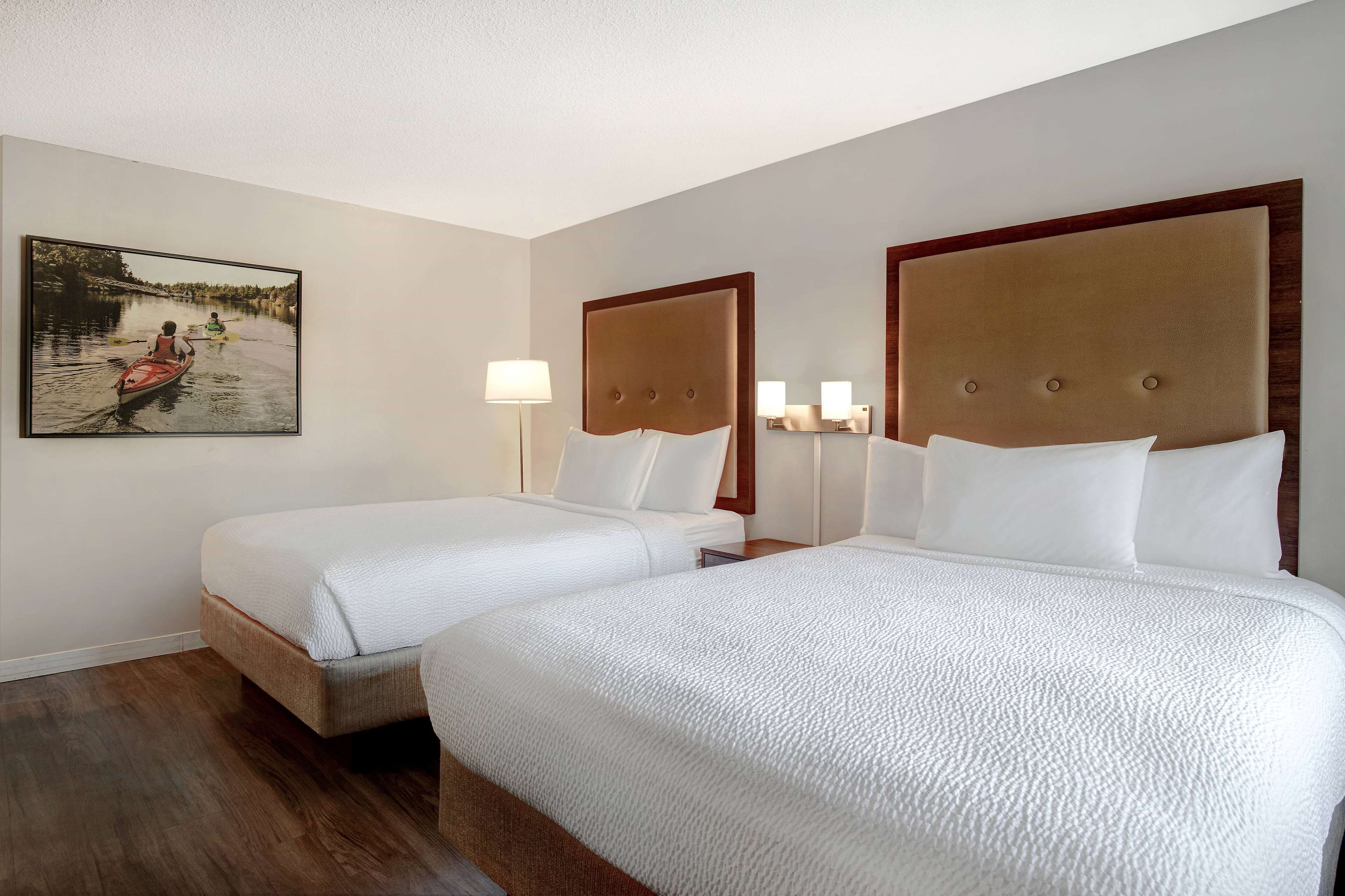 A hotel room with two beds, a painting on the wall, and a wooden floor.