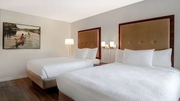 A hotel room with two beds, a painting on the wall, and a wooden floor.