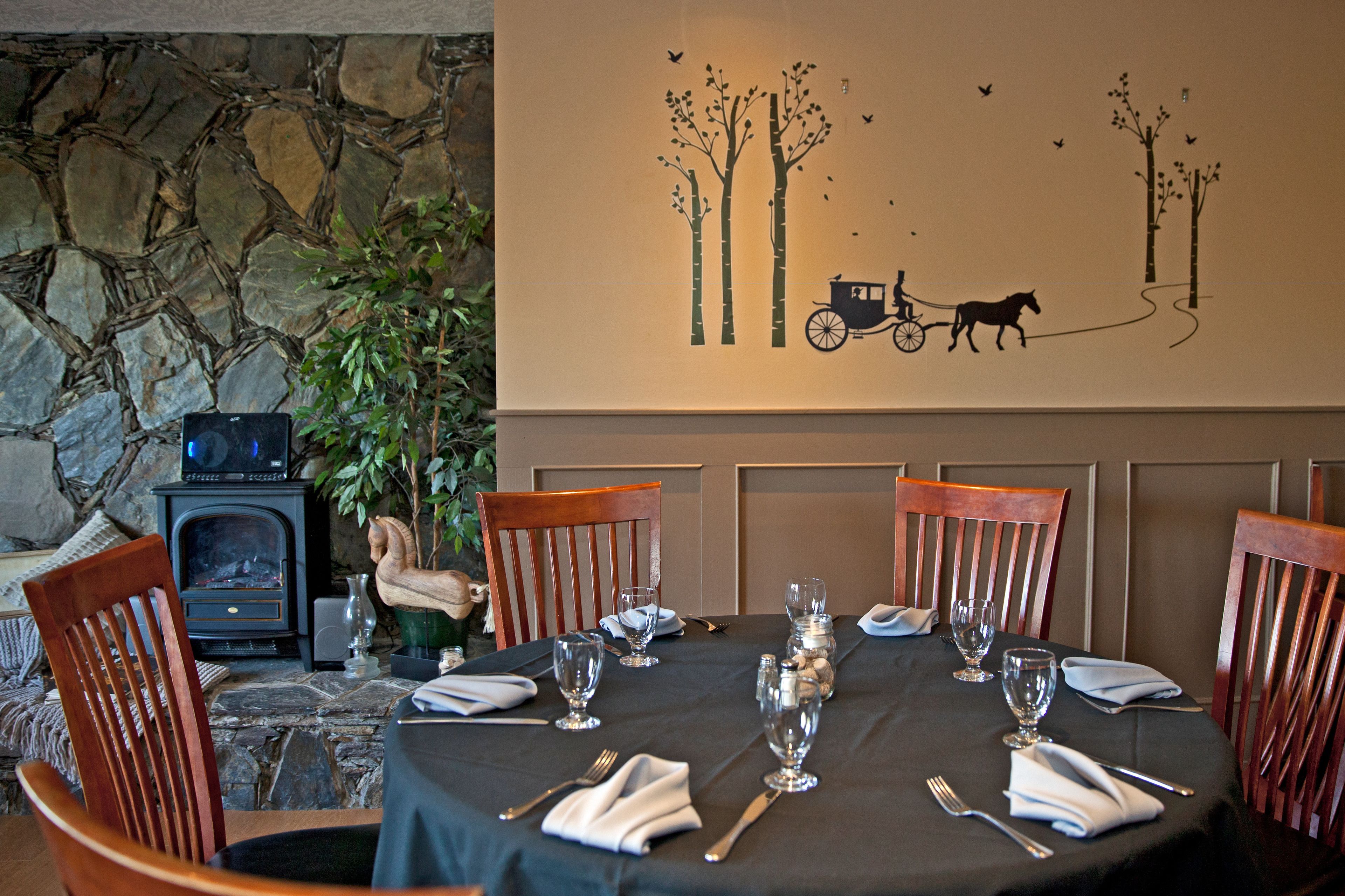 A dining table set for six with chairs, a stone wall, a fireplace, and a mural of trees and a horse-drawn carriage.