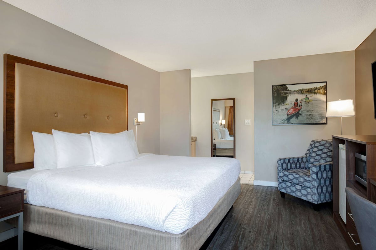Ein Hotelzimmer mit einem großen Bett, einem Sessel, einem Schreibtisch, einem Fernseher und einem Gemälde an der Wand.