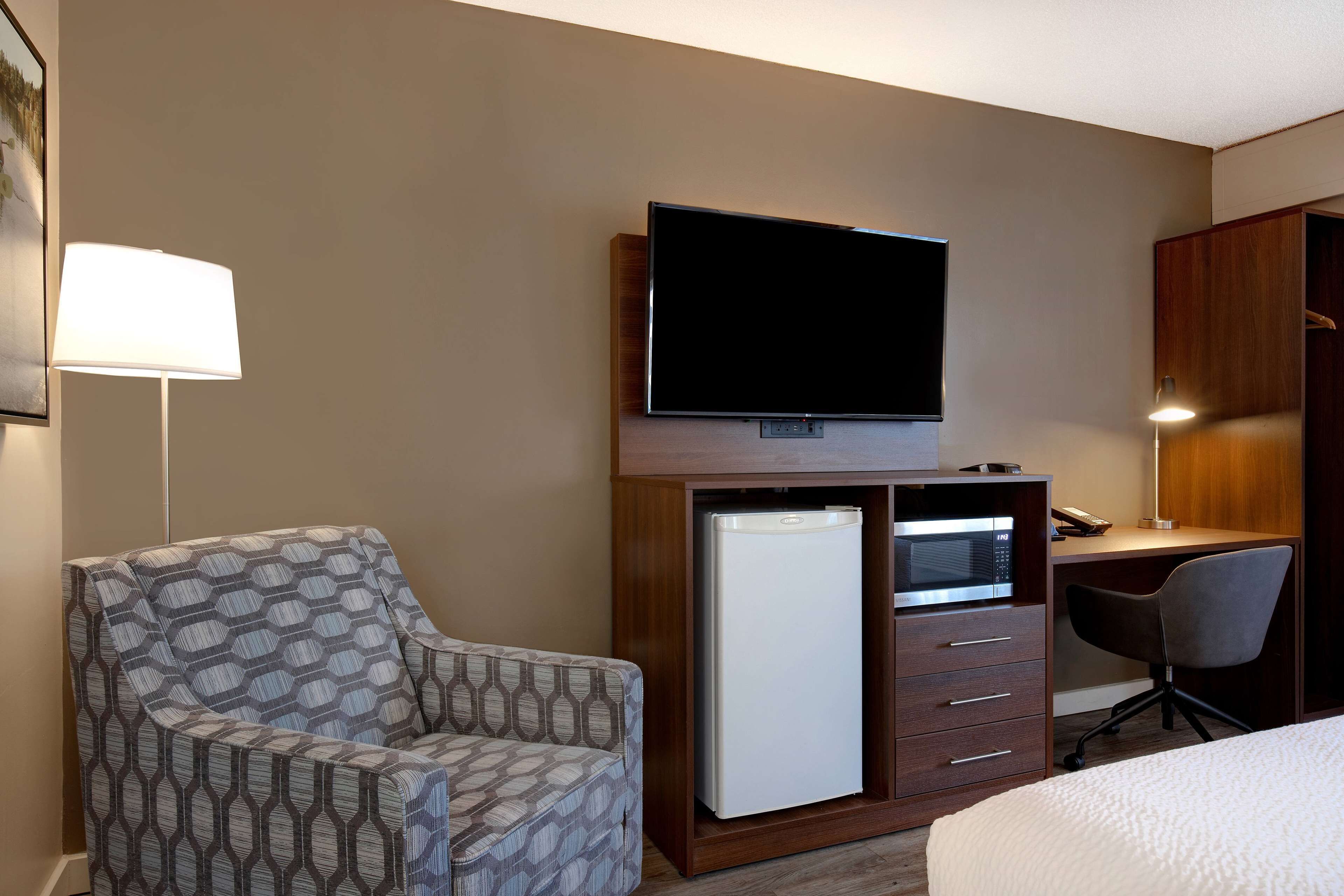 Una habitación de hotel con sofá, escritorio con computadora, televisión, refrigerador y lámpara.