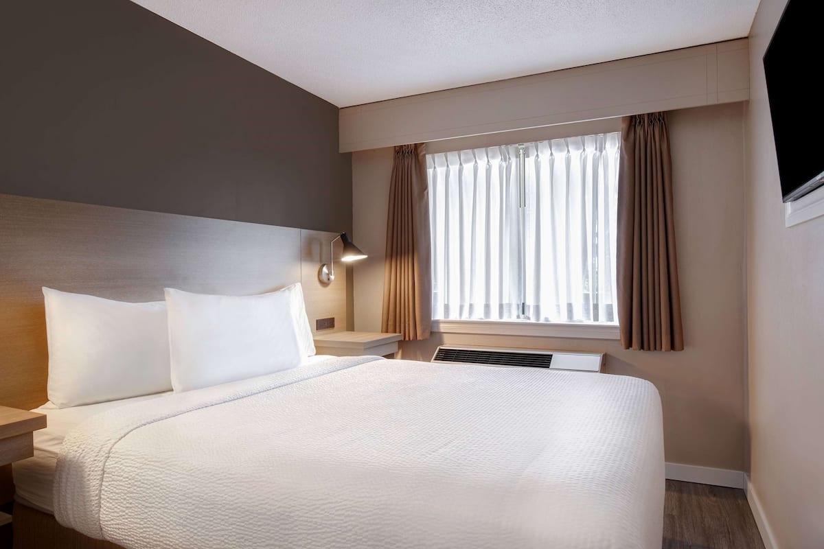 Ein Hotelzimmer mit einem großen Bett, einem Nachttisch, einer Lampe und einem Fenster mit Vorhängen.