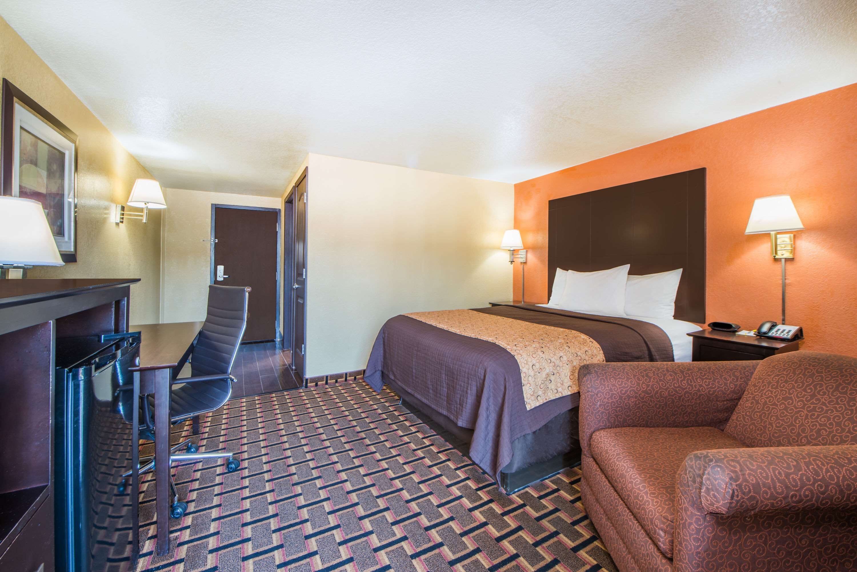 A hotel room with a bed, a desk, a chair, and a sofa.
