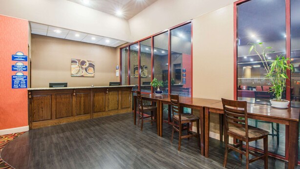 A hotel lobby with a reception desk, wooden chairs, a large window, and a potted plant. - Days Inn by Wyndham Joplin (Joplin)