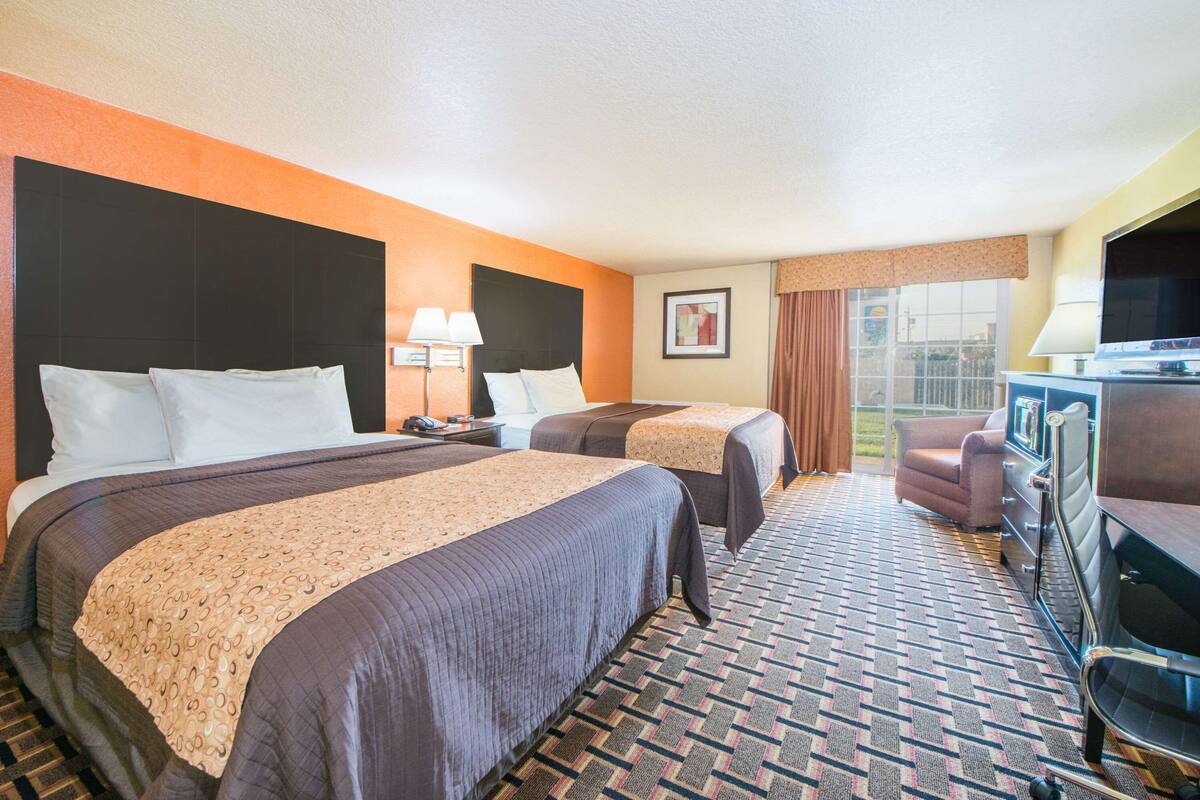 A hotel room with two beds, a TV, a desk, and a chair.