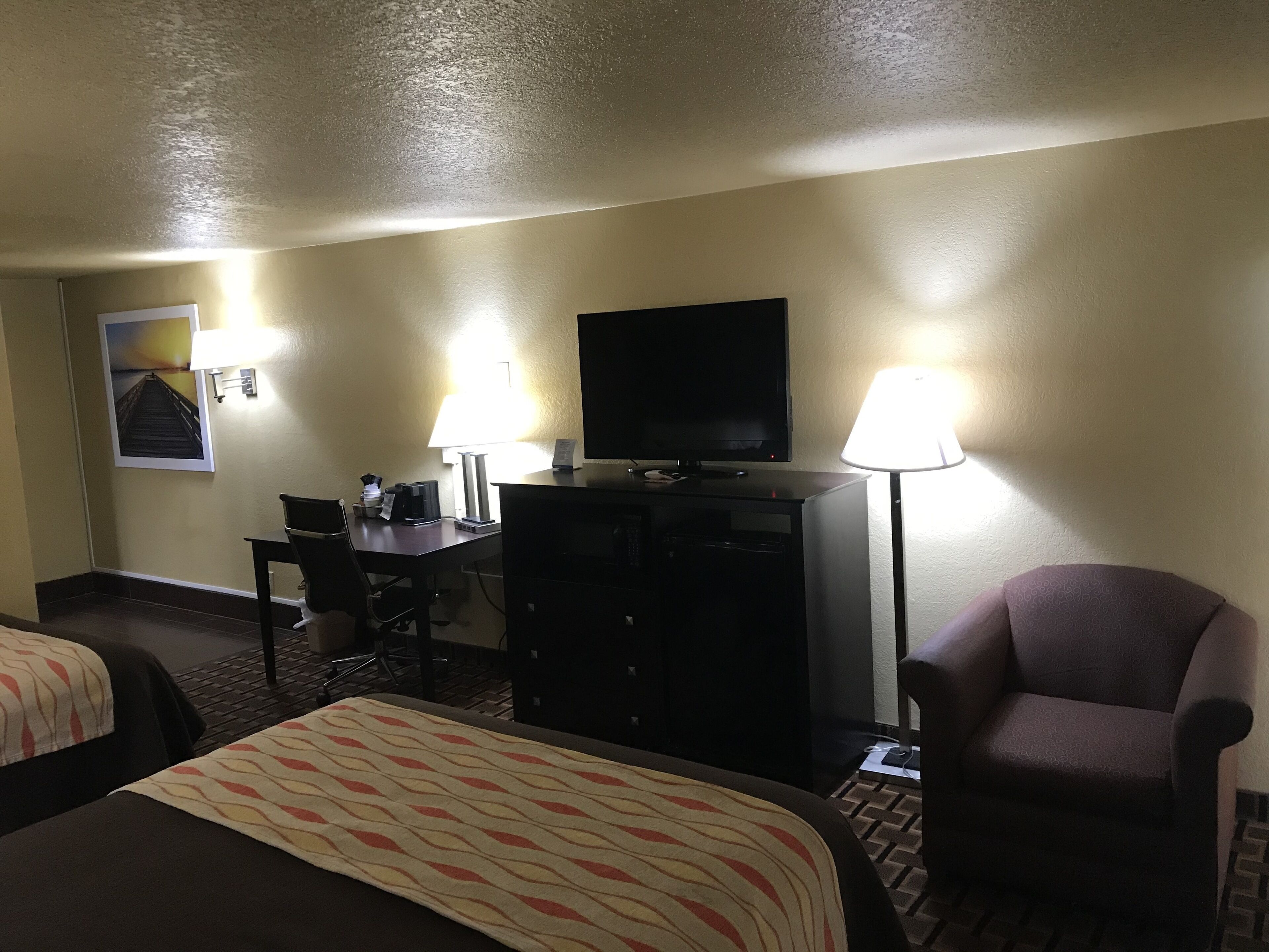 A hotel room with two beds, a desk with a computer, a TV, and two lamps.