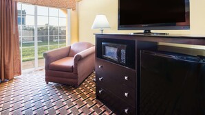 A hotel room with a large TV, a microwave, a sofa, and a patterned carpet. - Days Inn by Wyndham Joplin (Joplin)