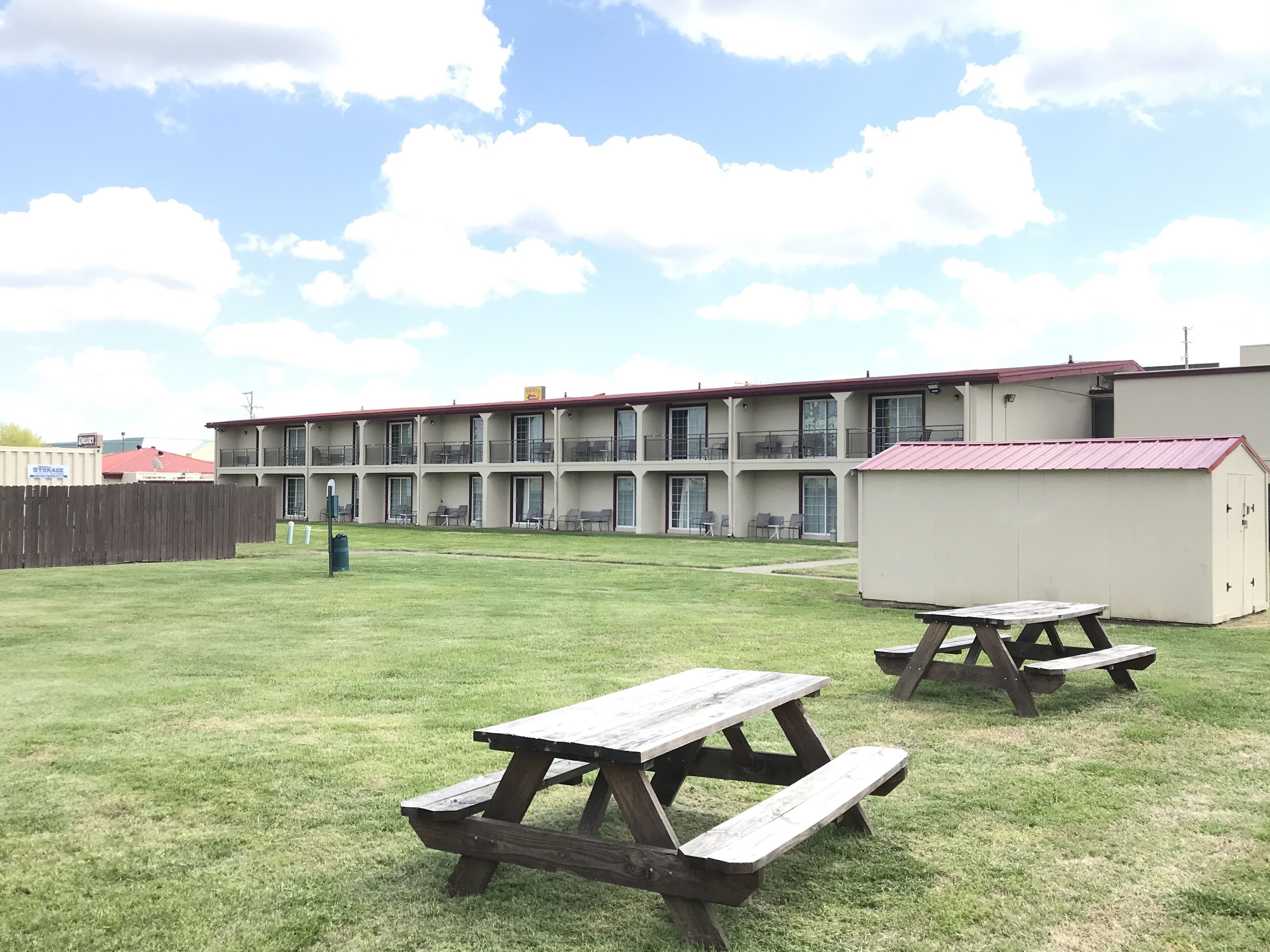 Un motel con patio cercado, mesas de picnic y un edificio con varios balcones.