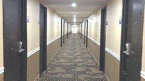 A long, narrow hallway with carpeted floors and doors on both sides, leading to a bright room at the end. - Days Inn by Wyndham Joplin (Joplin)