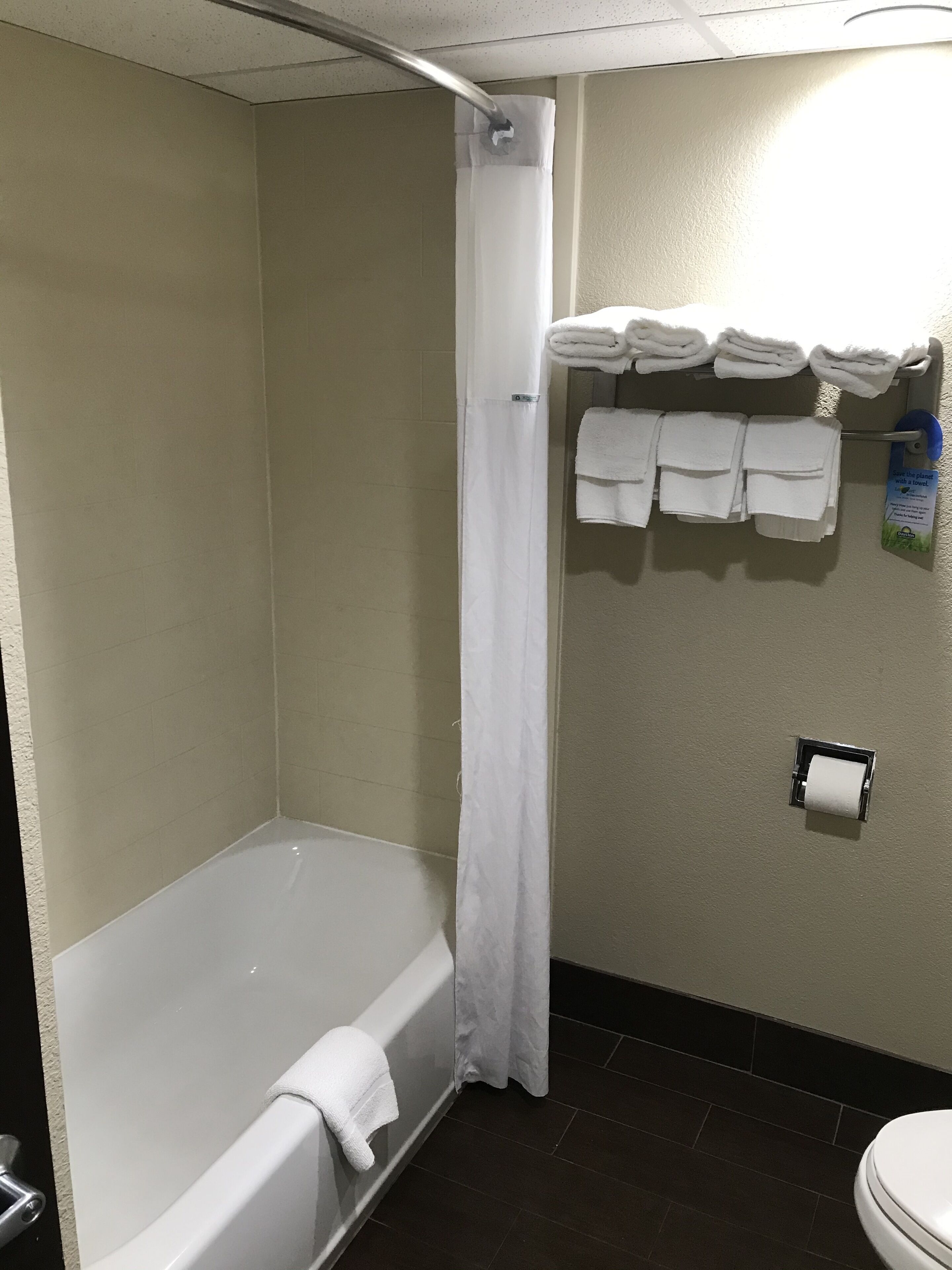 A bathroom with a bathtub, a shower curtain, a towel rack with towels, and a toilet paper holder.