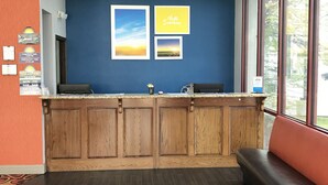 A reception area with a wooden counter, a blue wall with framed pictures, and a large window. - Days Inn by Wyndham Joplin (Joplin)