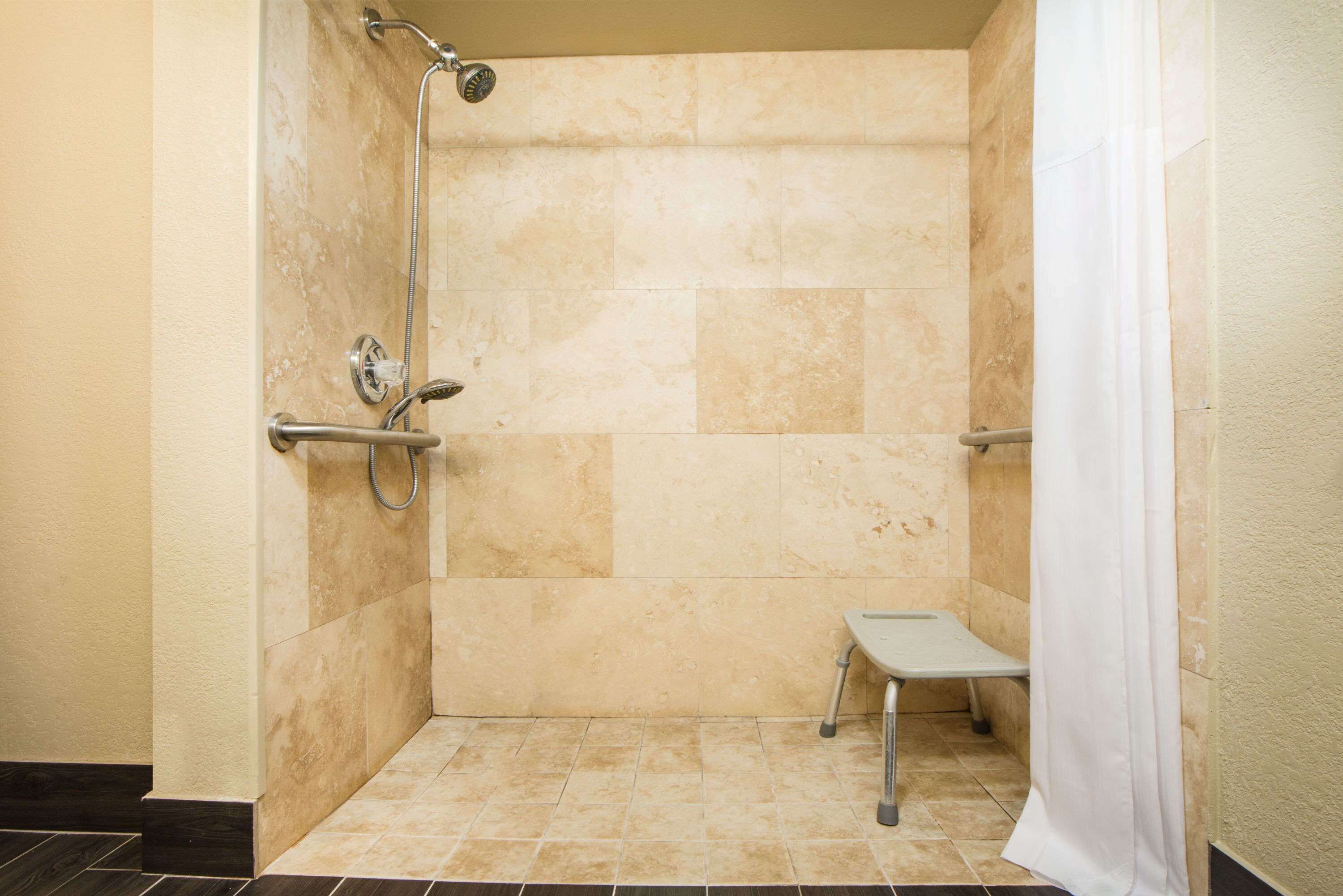 A shower area with beige tiles, a showerhead, a handheld shower, and a small bench.