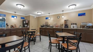 Uma cozinha de hotel com armários marrons, um espaço para café e uma área de refeições com mesas e cadeiras.