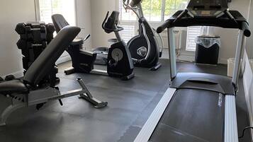 A gym with a treadmill, elliptical, and weight bench.