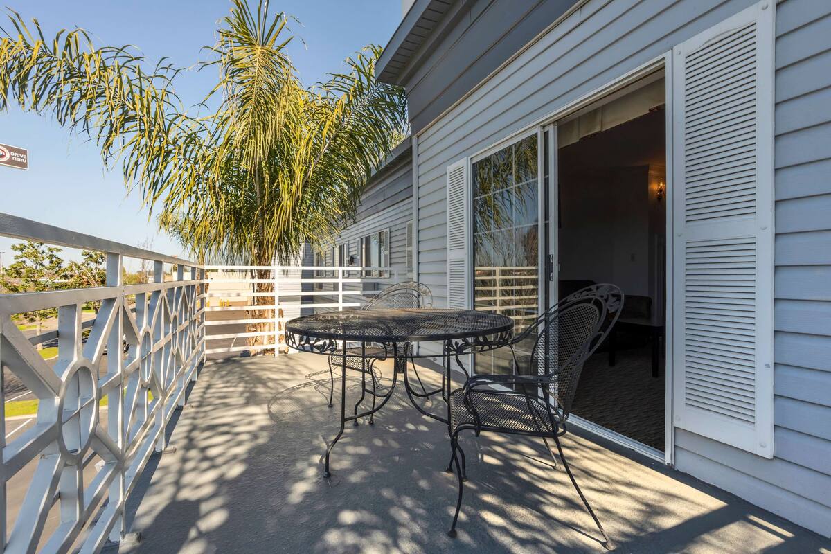 A covered patio with a metal table and chairs, a white railing, and a palm tree.