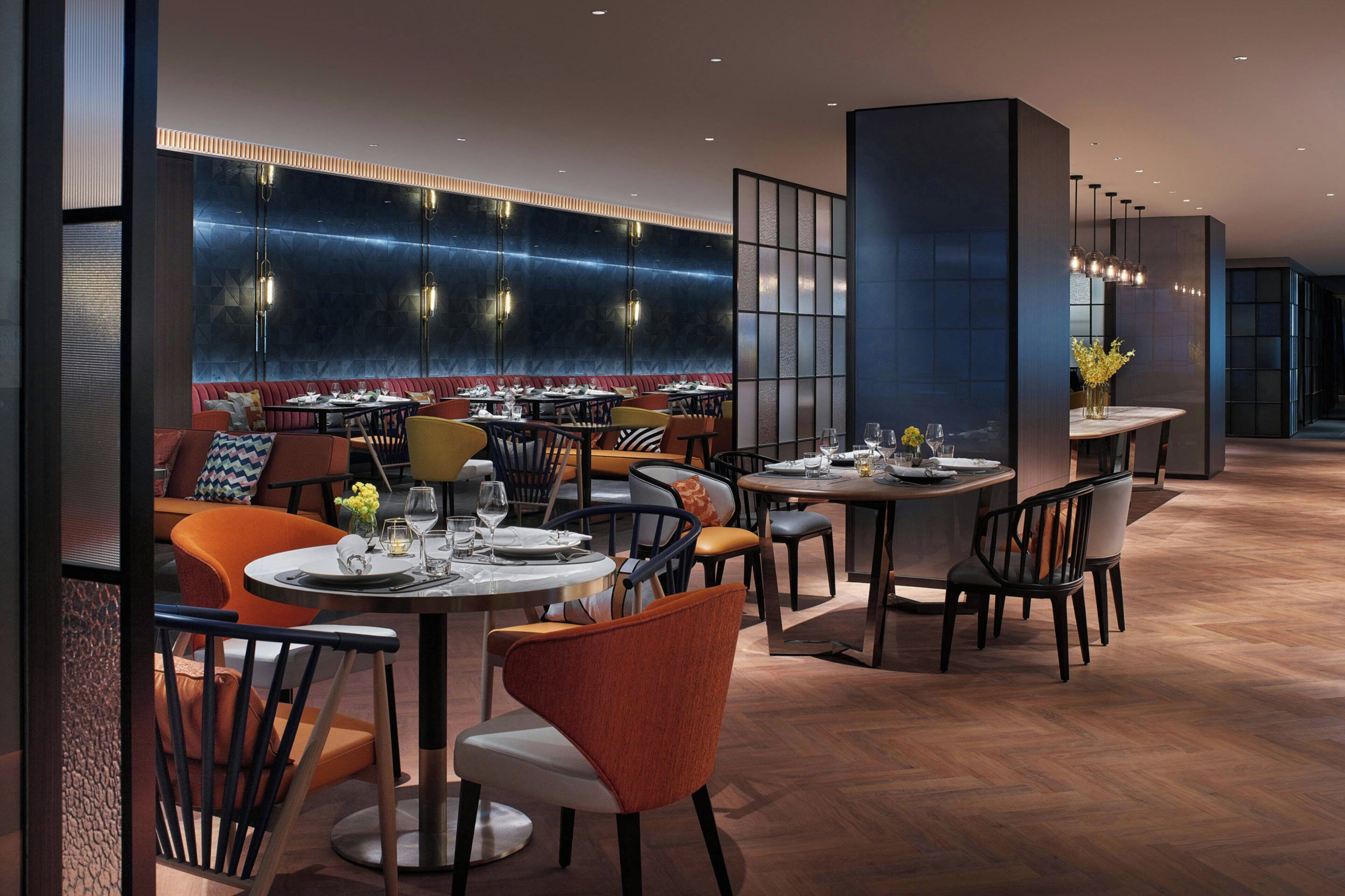 Ein modernes Restaurant mit runden Tischen, gepolsterten Sitzplätzen und einer Wand mit geometrischem Muster.