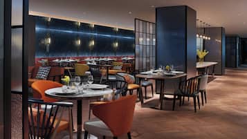 Ein modernes Restaurant mit runden Tischen, gepolsterten Sitzplätzen und einer Wand mit geometrischem Muster.