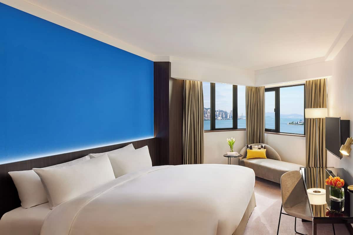 A hotel room with a large bed, a sofa, a desk, and a view of a cityscape.