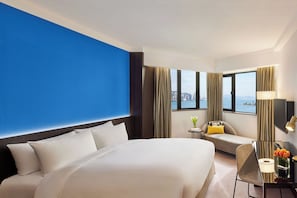 A hotel room with a large bed, a sofa, a desk, and a view of a cityscape.