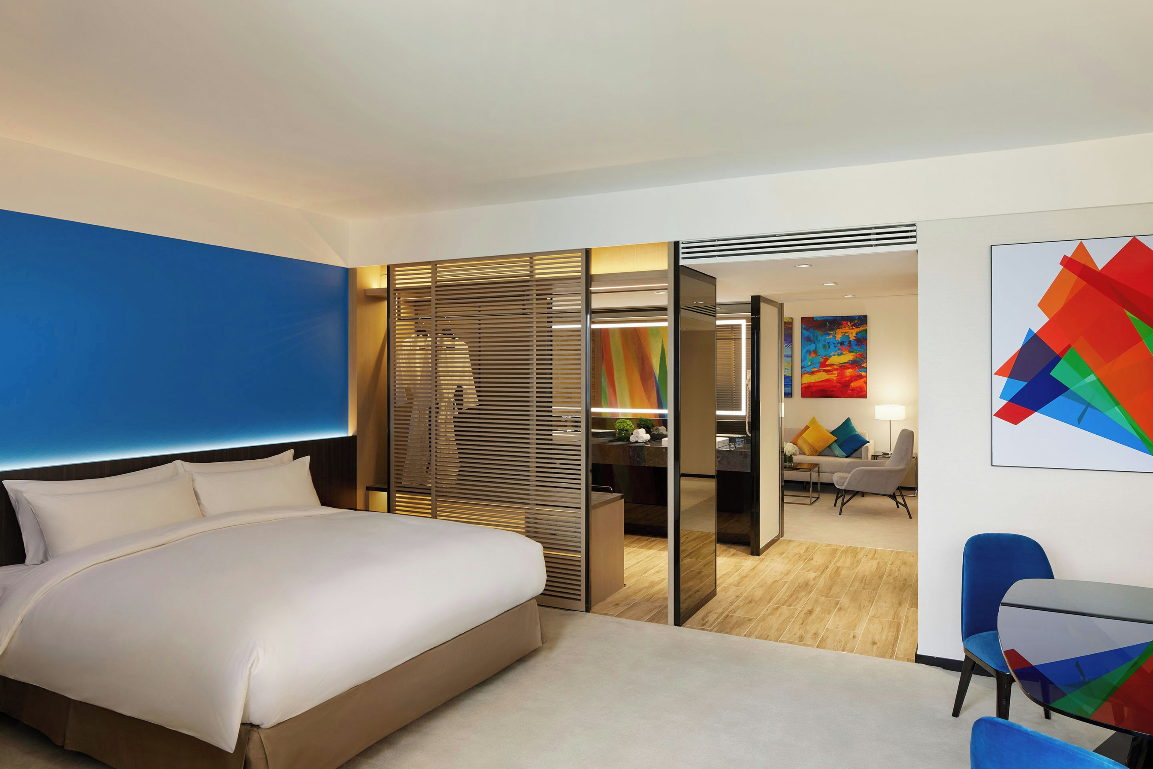 A hotel room with a bed, a desk, a chair, and a colorful abstract painting.