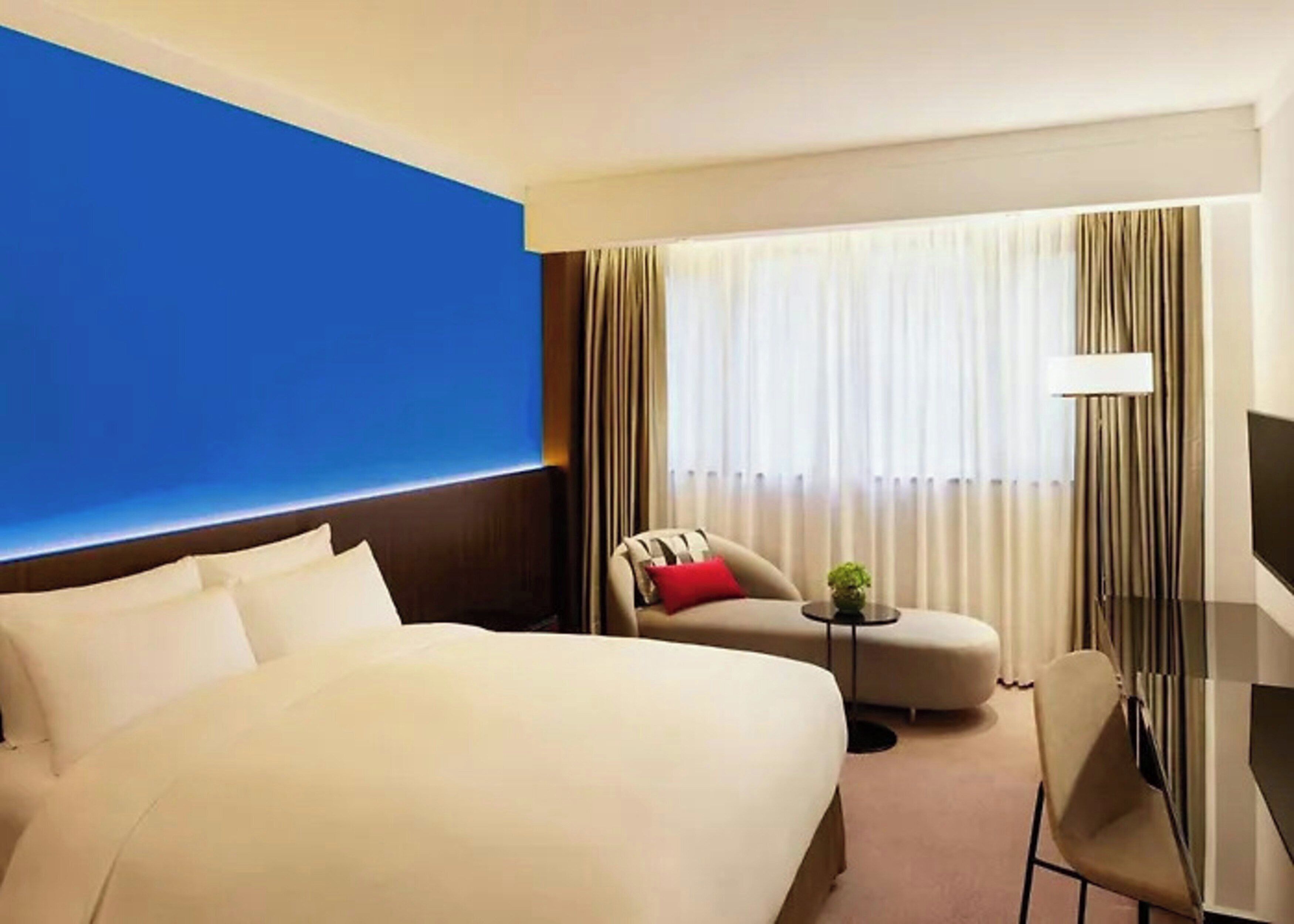 A hotel room with a large bed, a sofa, a chair, a small table, and a TV.
