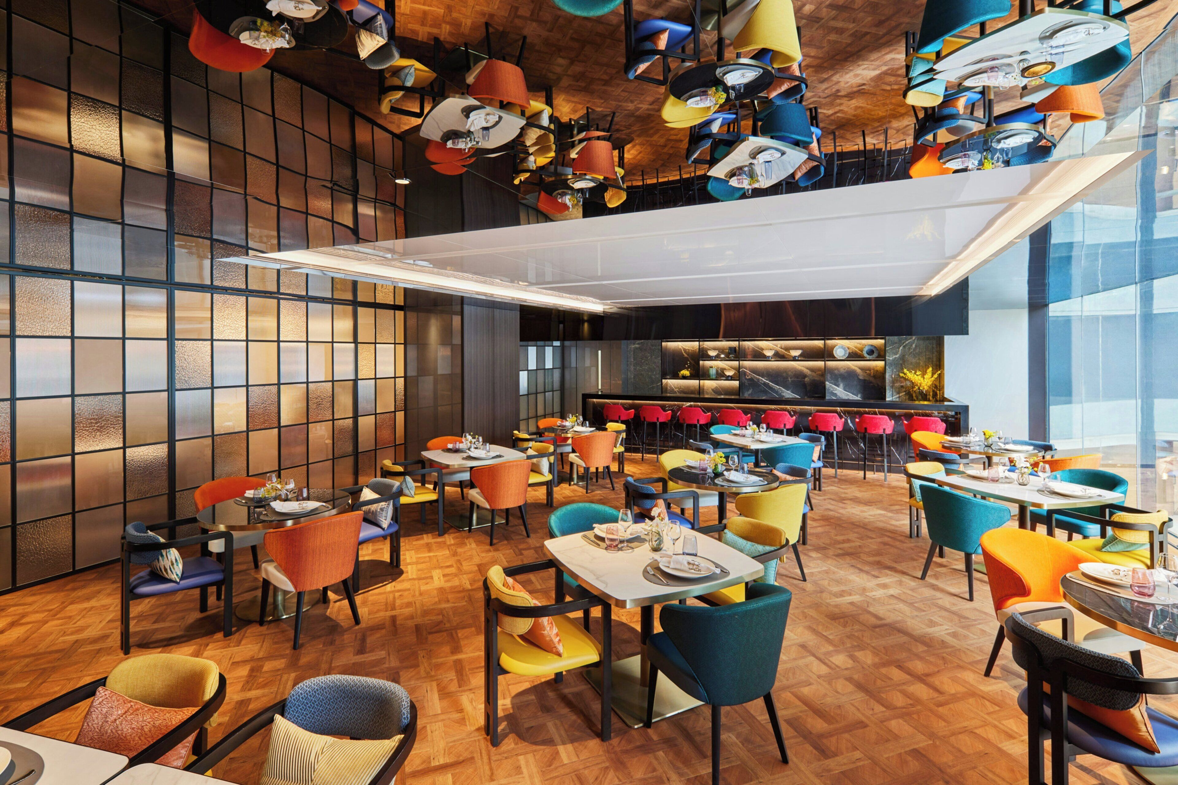 A modern restaurant with multiple dining areas, colorful chairs, and a variety of table settings.