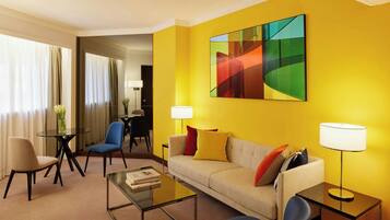 A hotel room with a sofa, armchairs, a coffee table, and a painting on the wall.