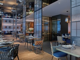 Interior de restaurante moderno con techos altos, divisiones de vidrio y mobiliario contemporáneo.
