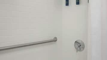 Ein hell gefliestes Badezimmer mit einer Badewanne, einer Handstange, einem Duschkopf und zwei Toilettenartikeln.