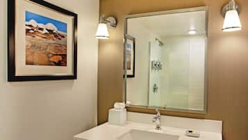 Un bagno con uno specchio grande, un lavandino, un quadro incorniciato e due luci a parete.