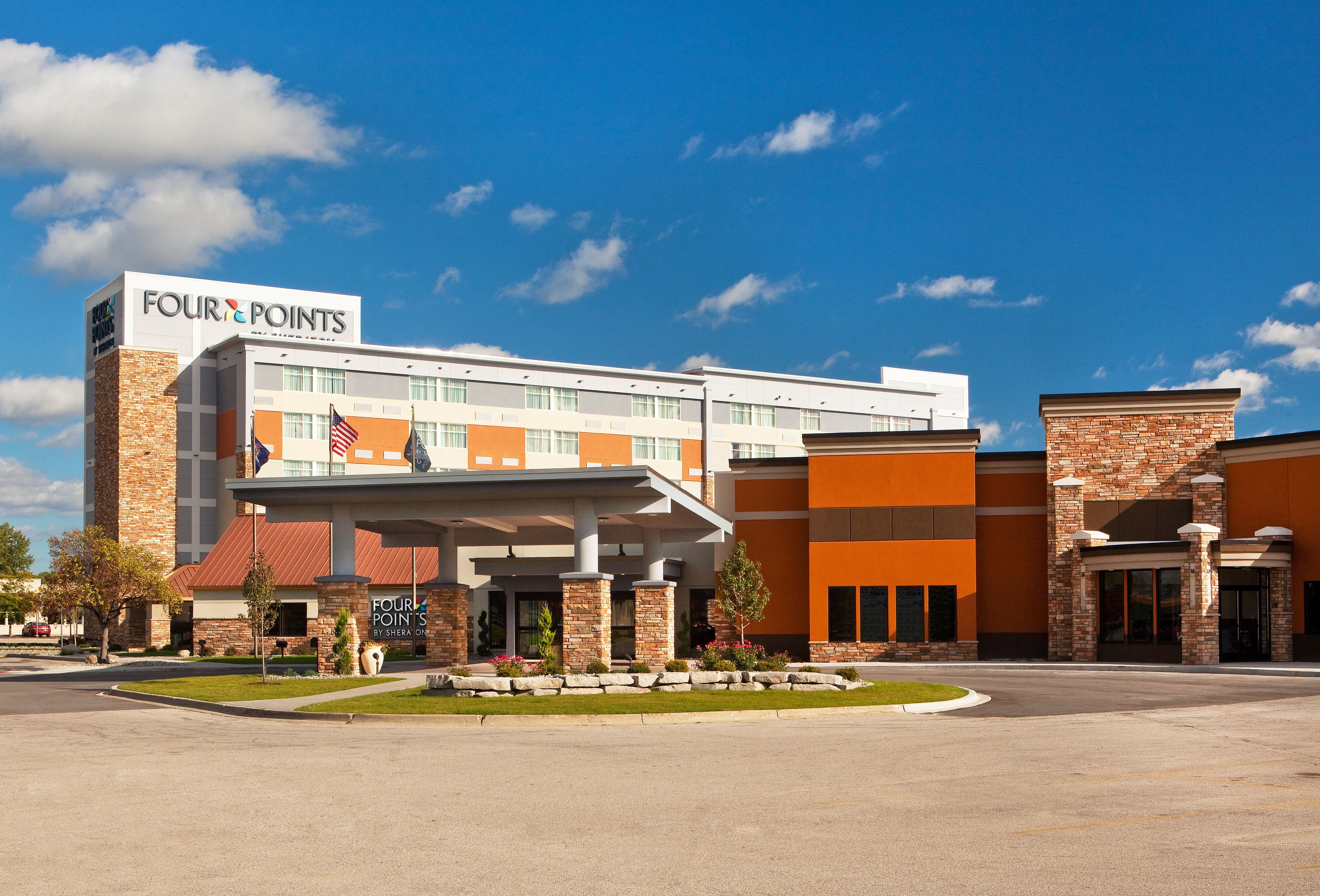 Un hotel Four Points dal design moderno, con un ingresso ben visibile e un'area verde piantumata di fronte.