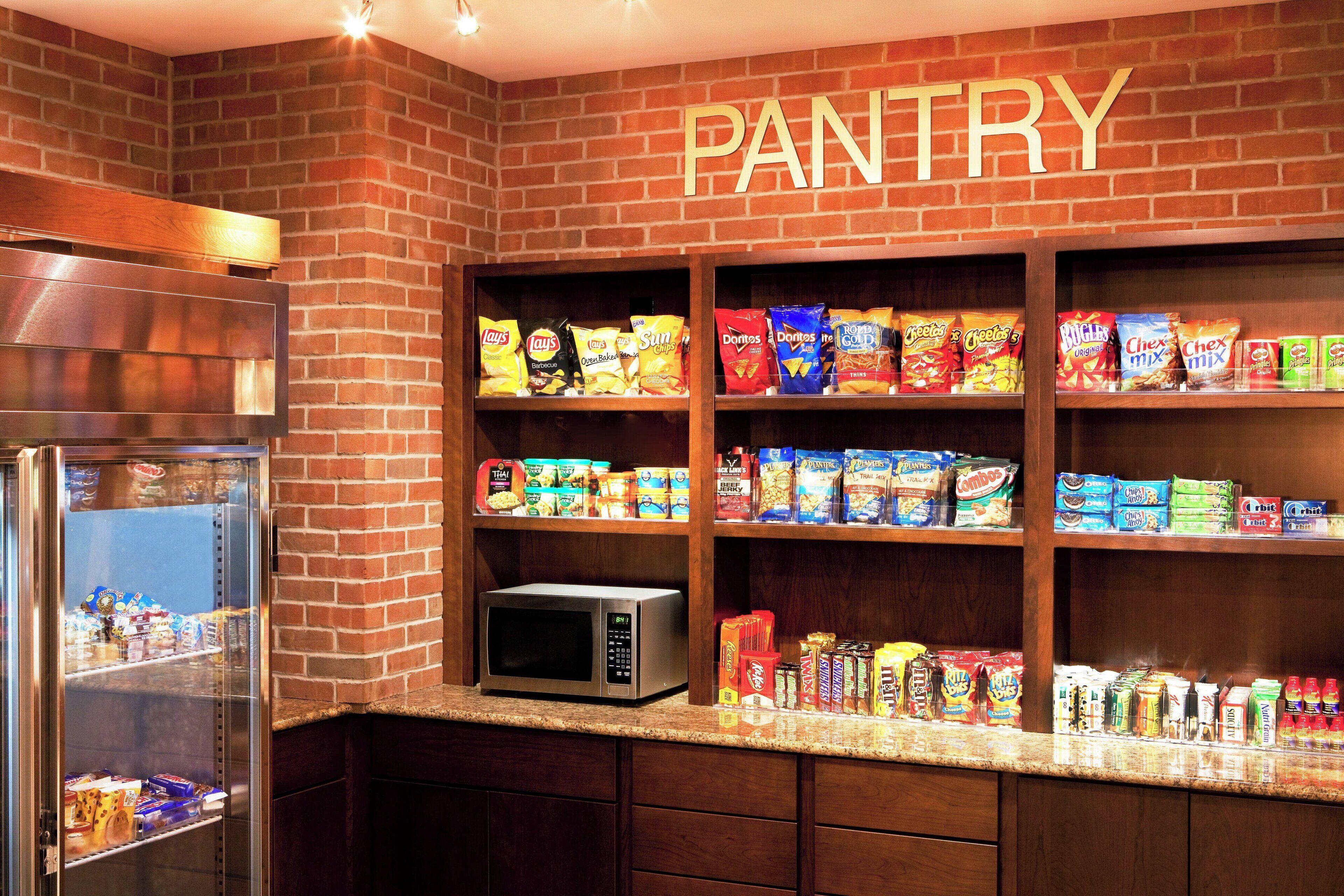 A pantry with shelves stocked with snacks and a microwave.