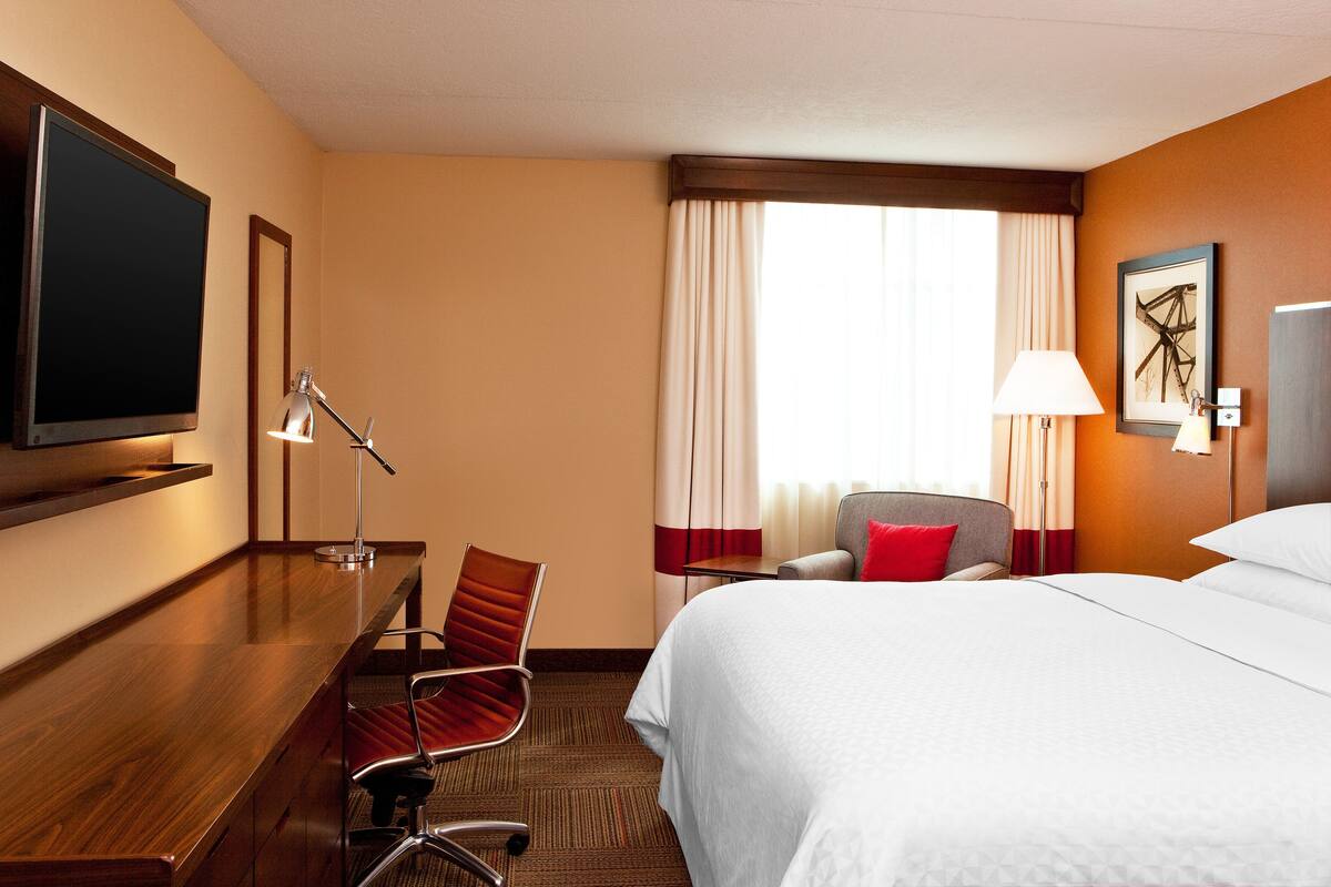 A hotel room with a bed, a desk, a chair, a TV, and a window with curtains.