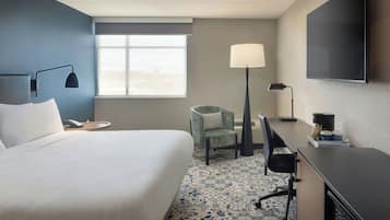 A hotel room with a large bed, a desk, a chair, a TV, and a window with a view.