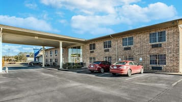 A gas station with two cars parked, a covered canopy, and a brick building with multiple windows.