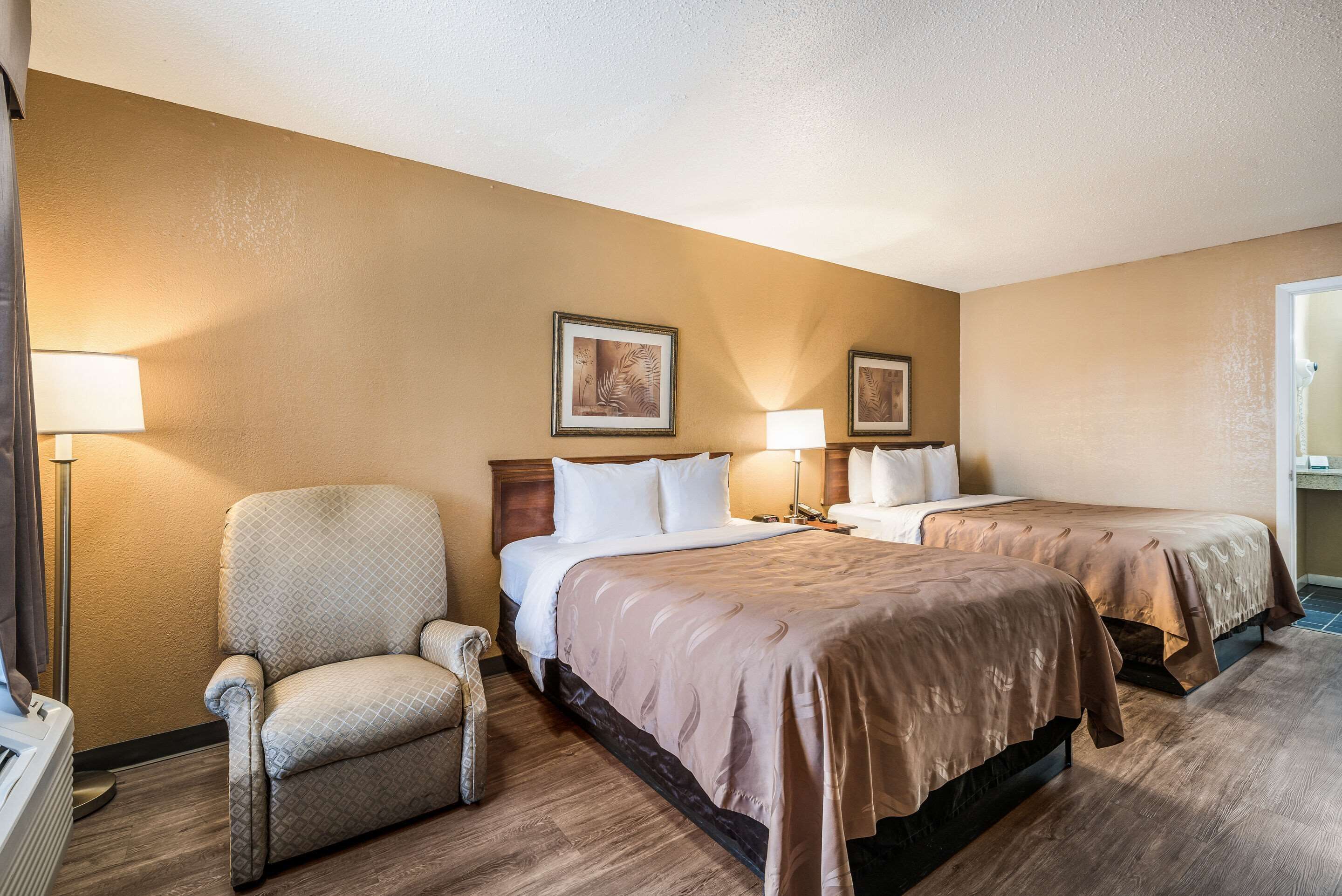 Habitación de hotel con dos camas, una silla y dos lámparas.