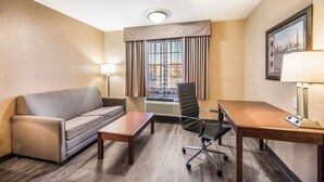 A hotel room with a sofa, a desk, a chair, a lamp, and a window with curtains. - Quality Inn Arkadelphia - University Area (Caddo Valley)