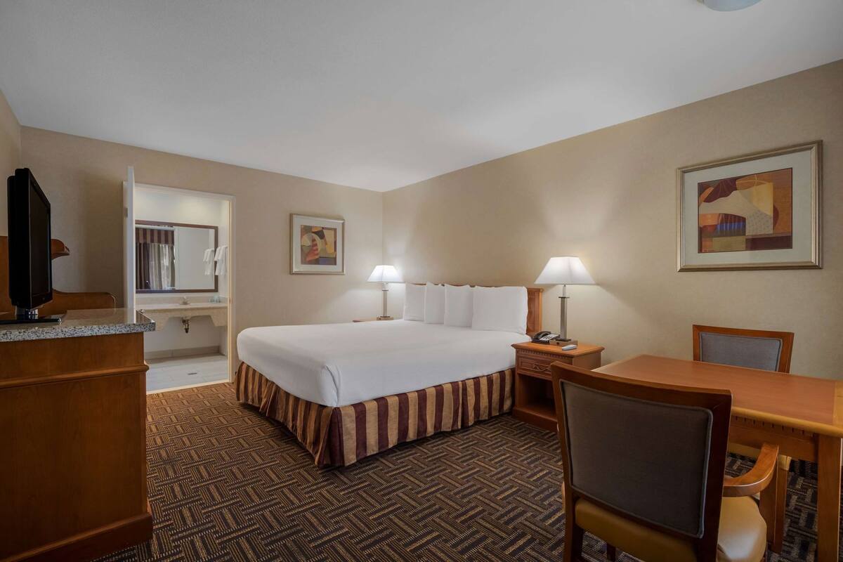A hotel room with a bed, desk, chair, lamp, and a television.