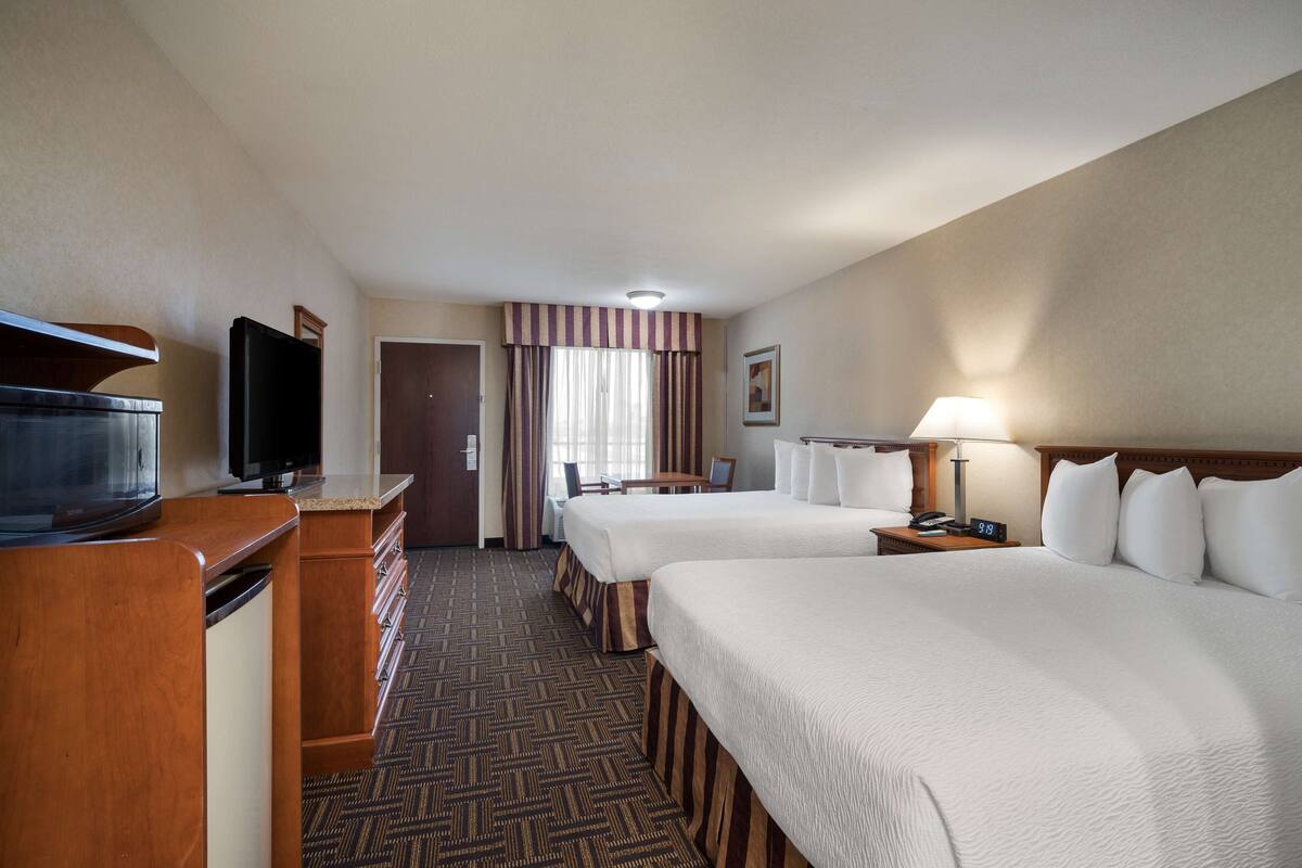 A hotel room with two beds, a television, a desk, and a lamp.
